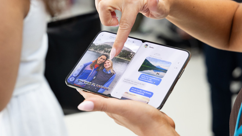 An unfolded iPhone Duo with a finger pointing at a photo on the left side and messages on the right.